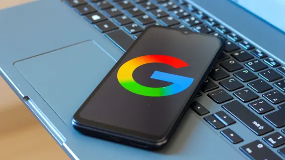 Ein Handy liegt auf einer Laptoptastatur. Das Display zeigt das Google Logo