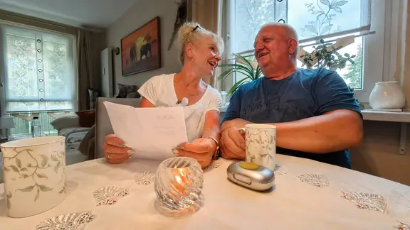 Eine blonde Frau und ein älterer Mann sitzen gemeinsam am Tisch. 