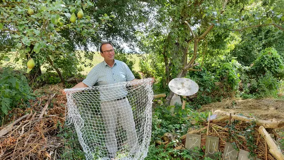 Ein Mann im Grünen vor Bäumen mit einem Netz in der Hand