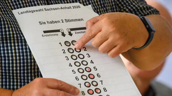 Ein Mitglied vom Blinden und Sehbehindertenverband Sachsen-Anhalt erklärt die Wahlschablonen für blinde und sehbehinderte Menschen. 