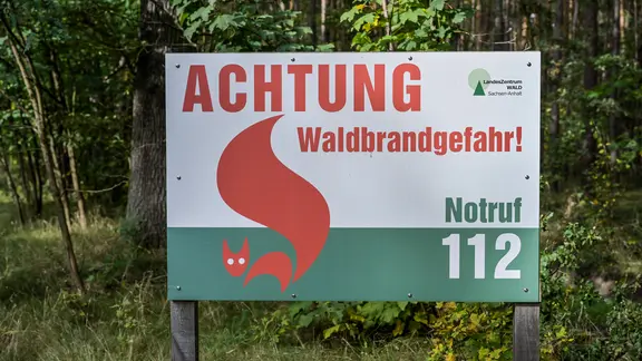 Ein Schild vor einem Wald mit der Aufschrift "Achtung Waldbrandgefahr".