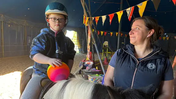 Eine Frau führt ein Pferd, auf dem ein Junge sitzt 