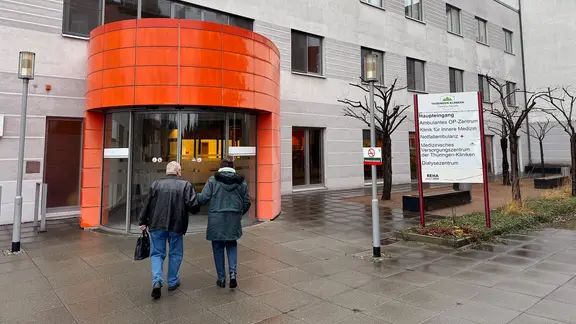 Ein Mann und eine Frau gehen auf den Haupteingang des Thüringen Klinikums/MVZ in Pößneck zu.