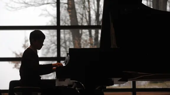 Silhouette vor großer Fensterfront: Ein Junge spielt auf einem Flügel im Festsaal des Musikgymnasiums Schloss Belvedere in Weimar.