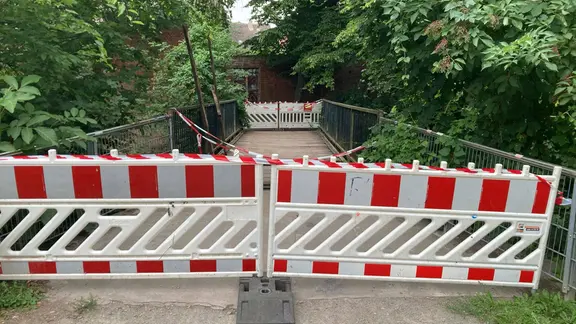 Eine Brücke im Grünen ist mit rot-weißen Barken gesperrt