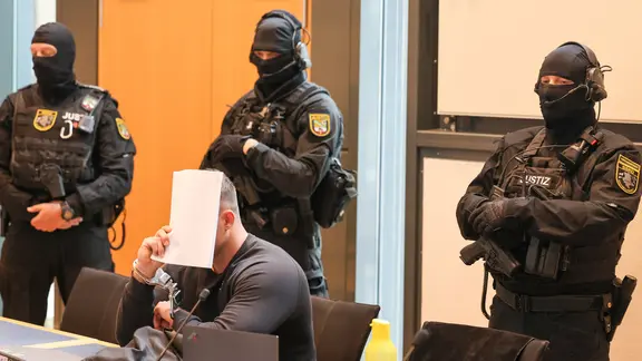 Der Angeklagte im Prozess um Fußball-Krawalle in Magdeburg umringt von Polizisten am 20.7.26