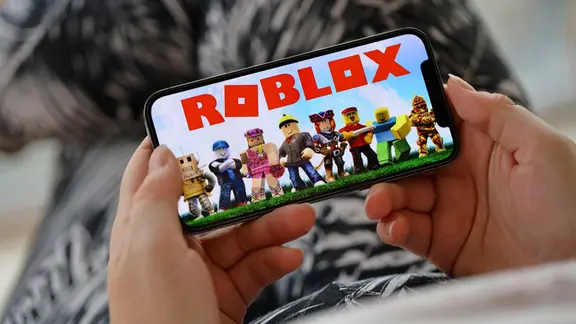 Ein Kind hält ein Handy in der Hand, auf dem der "Roblox"-Schriftzug zu sehen ist.