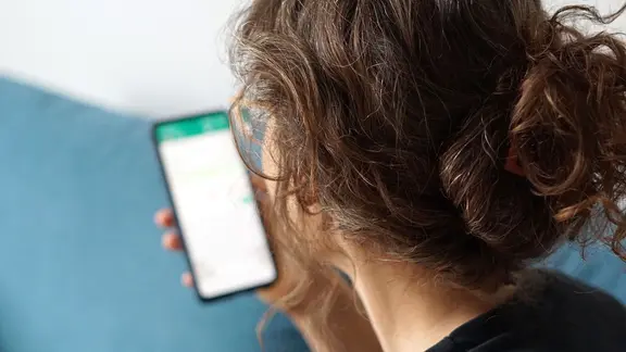 Eine Frau hält ihr Smartphone in der Hand und liest eine Whatsapp-Nachricht.