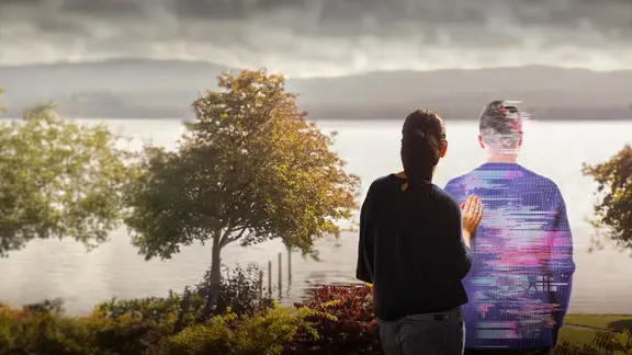 Ein Mann, halb in digitalen Fragmenten dargestellt, steht neben mit einer Frau vor einer graubewölkten Landschaft.