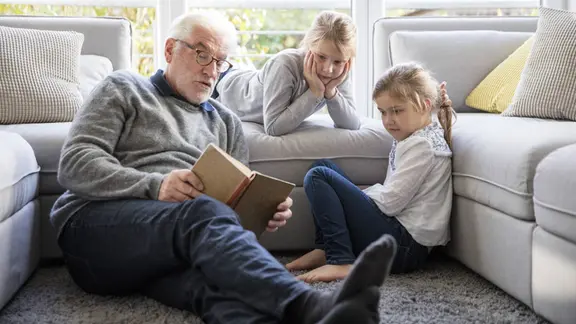 Zwei Mädchen und ihr Großvater lesen im Wohnzimmer ein Buch