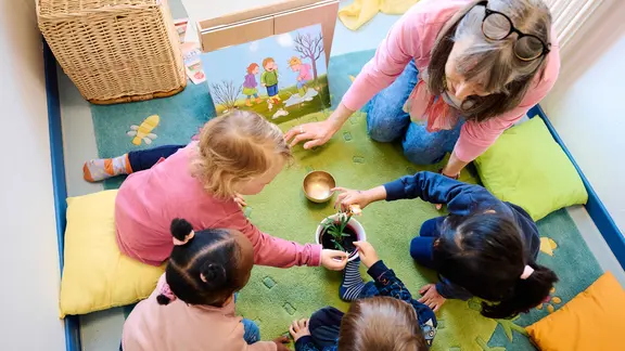 Kitaerzieherin mit einer kleinen Gruppe von Kindern, die im Kreis sitzen