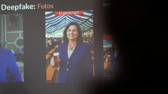 Auf einer Präsentation ist ein mit Hilfe von KI erstelltes Deepfake von Landtagspräsidentin Aigner zu sehen. Es zeigt sie mit einem Glas Bier in der Hand. 