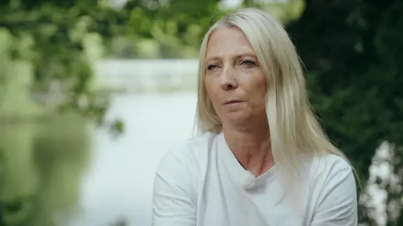 Frau mit blonden Haaren und weißem T-Shirt in einem Park mit See: Autorin Manuela Müller