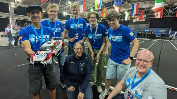 Ein Team bei einem Modellauto-Wettbewerb schaut begeistert in die Kamera.