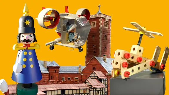 Spielzeugfiguren und -fahrzeuge vor einer historischen Backsteinburg mit Türmen.