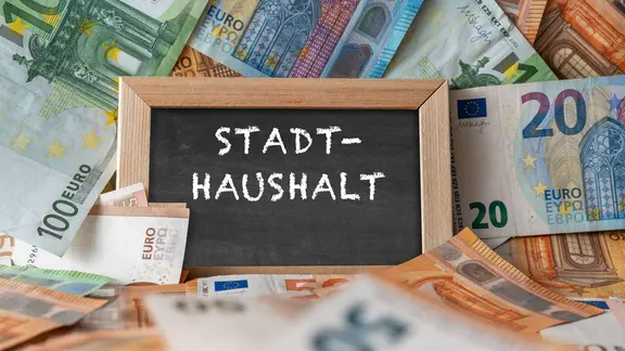 Ein Schild mit der Aufschrift "Stadthaushalt" liegt zwischen Euro-Banknoten.