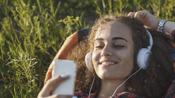 Teenagerin liegt auf einer Wiese und hört Musik mit Kopfhörern