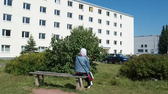 Ein Frau mit Kopftuch sitzt in Suhl vor einem Wohnheim der Erstaufnahmestelle auf einer Bank.