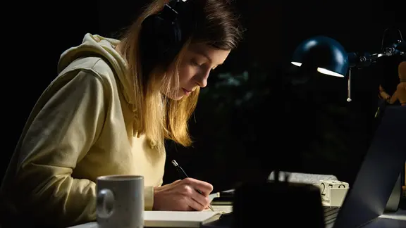 Frau, die nachts mit Kopfhörern Musik hört und am Laptop arbeitet.