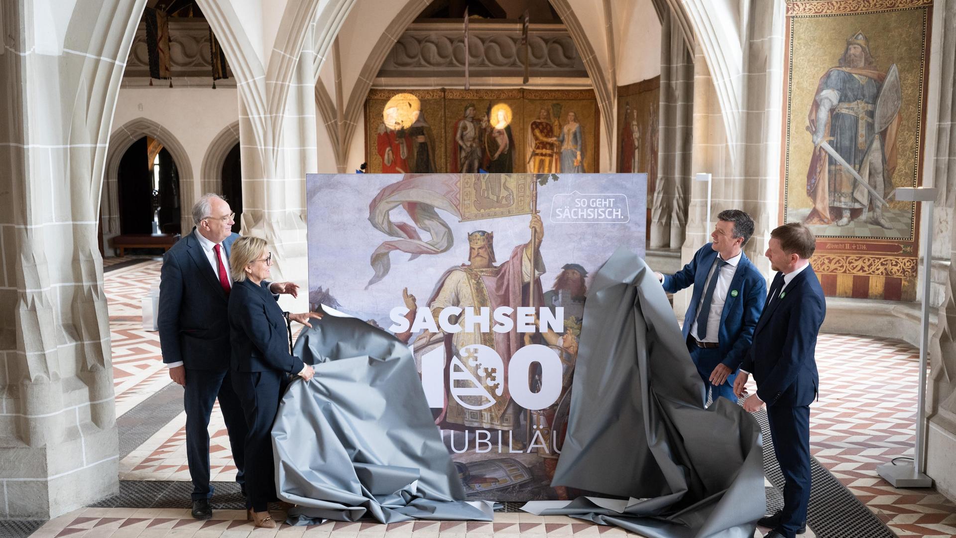 Christian Striefler, Barbara Klepsch, Markus Renner und Michael Kretschmer enthüllen in der Albrechtsburg Meißen ein Plakat für die bevorstehende Landesausstellung 