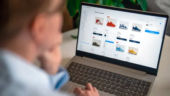 Eine Frau, die auf einer E-Commerce-Website mit ihrem Laptop Turnschuhe aussucht.