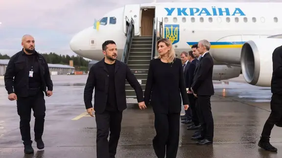 Der ukrainische Präsident Selenskyj steht mit weiteren Personen vor einem Flugzeug, das mit ukrainischer Flagge bemalt ist. 