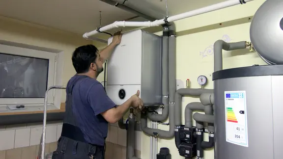 Ein Handwerker befestigt die Abdeckung an einer Steuereinheit einer Wärmepumpe im Keller einer Doppelhaushälfte.