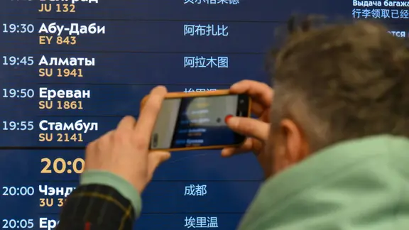 Mann fotografiert am Flughafen eine elektronische Anzeige mit Abflugzeiten