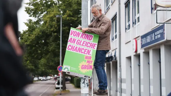 Ein Mann hängt ein Wahlplakat auf.