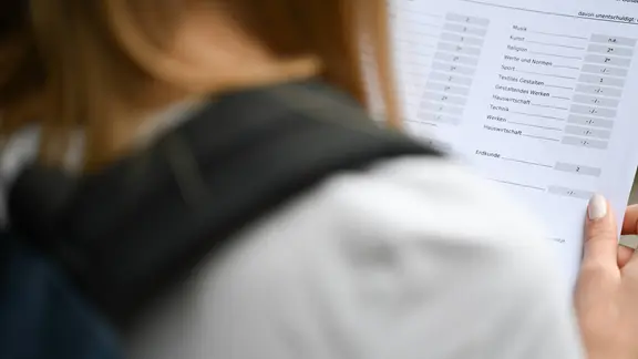 Eine Schülerin hält ein Zeugnis in der Hand.