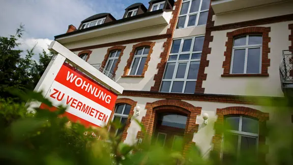 Ein Schild mit der Aufschrift Wohnung zu vermieten vor einem Wohnhaus.