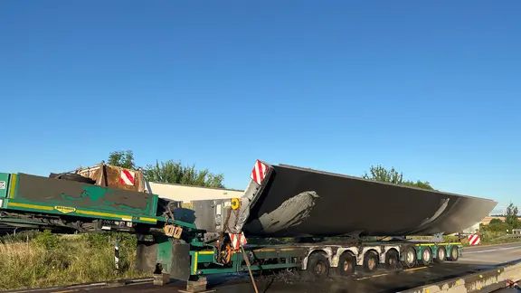 Ein verunglückter Schwertransport, der Windradteile geladen hat, steht am Straßenrand.