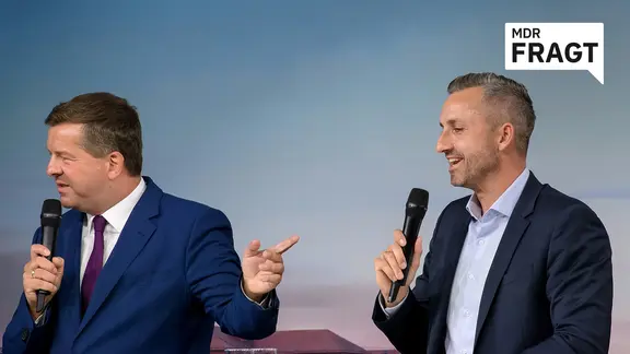 Zwei Männer diskutieren auf einer Bühne vor einer Bildwand.