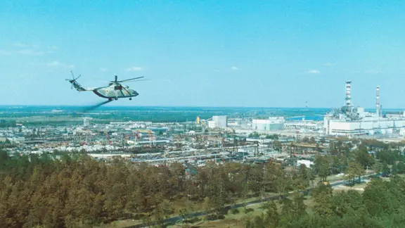 Hubschrauber über Industrieanlage mit Reaktorgebäude und Schornsteinen, Blick aus der Höhe.