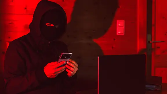 Ein maskierter Betrüger nutzt ein Smartphone.