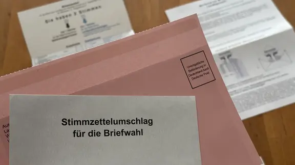 Hand hält Umschlag für Stimmzettel zu Briefwahl, Stimmzettel liegt darunter