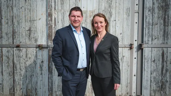 Thomas Schulze und Claudia Wittig stehen vor einem alten Holztor.