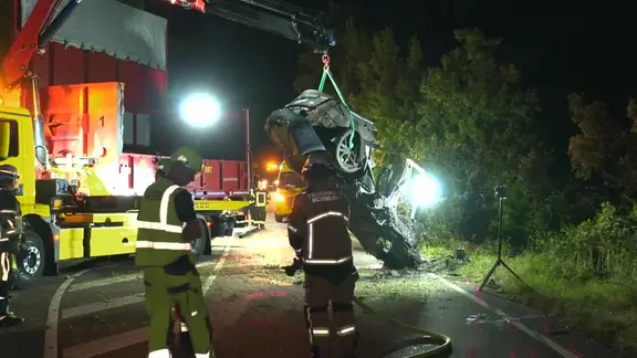 Ein völlig zerstörtes Auto wird nach einem Unfall aus Büschen geborgen und abgeschleppt.