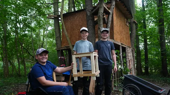 Lukas, Levi und Leo posieren mit ihrem neuen Stuhl vor dem Baumhaus.