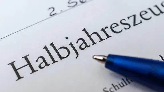 Eine ausschnitthafte Nahaufnahme zeigt ein Zeugnis auf dem ein Kugelschreiber liegt.