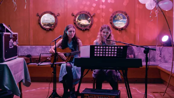 Szene aus dem Film "Etwas ganz Besonderes": Zwei Mädchen machen zusammen in einem rot beleuchteten Partyraum Musik. Eine spielt Gitarre, die andere Keyboard.