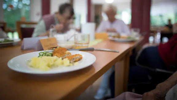 Bewohner in einem Altenpflegeheim sitzen beim Mittagessen in dem Essensraum