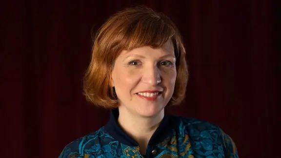Lena Liberta, eine Frau mit kinnlangen, rötlichen Haaren, lacht in die Kamera.