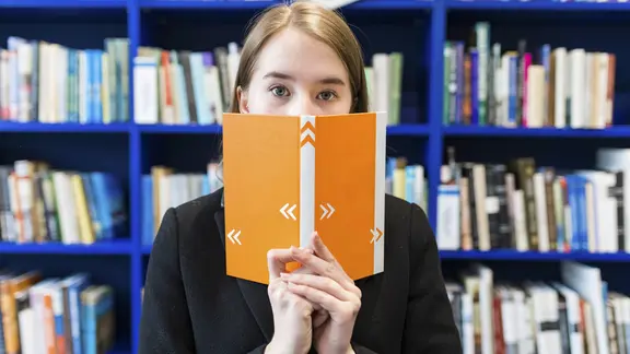 Frau versteckt mit ernster Miene ihr Gesicht hinter einem Buch.
