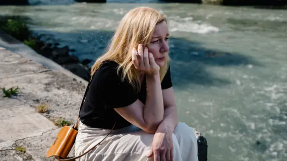 Eine Frau sitzt an einem Flussufer.