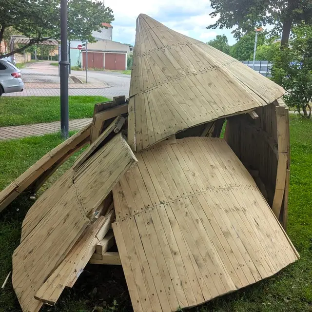 Ein zerstörtes Kunstwerk aus Holz auf einer Wiese.