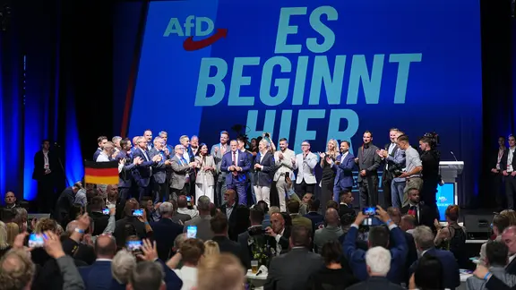 Funktionäre der AfD stehen bei der Wahlparty der AfD im Alten Theater vor dem Schriftzug "Es beginnt hier" auf der Bühne.
