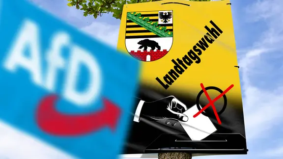 Eine blaue Fahne der AfD weht vor einem Plakat zur Wahl in Sachsen-Anhalt.