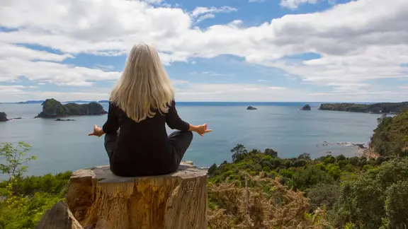 Ältere Frau meditiert auf einer Klippe nahe des Ozenas, Neuseeland.