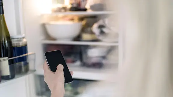 Eine Frau steuert ihren intelligenten Kühlschrank mit einem Smartphone.